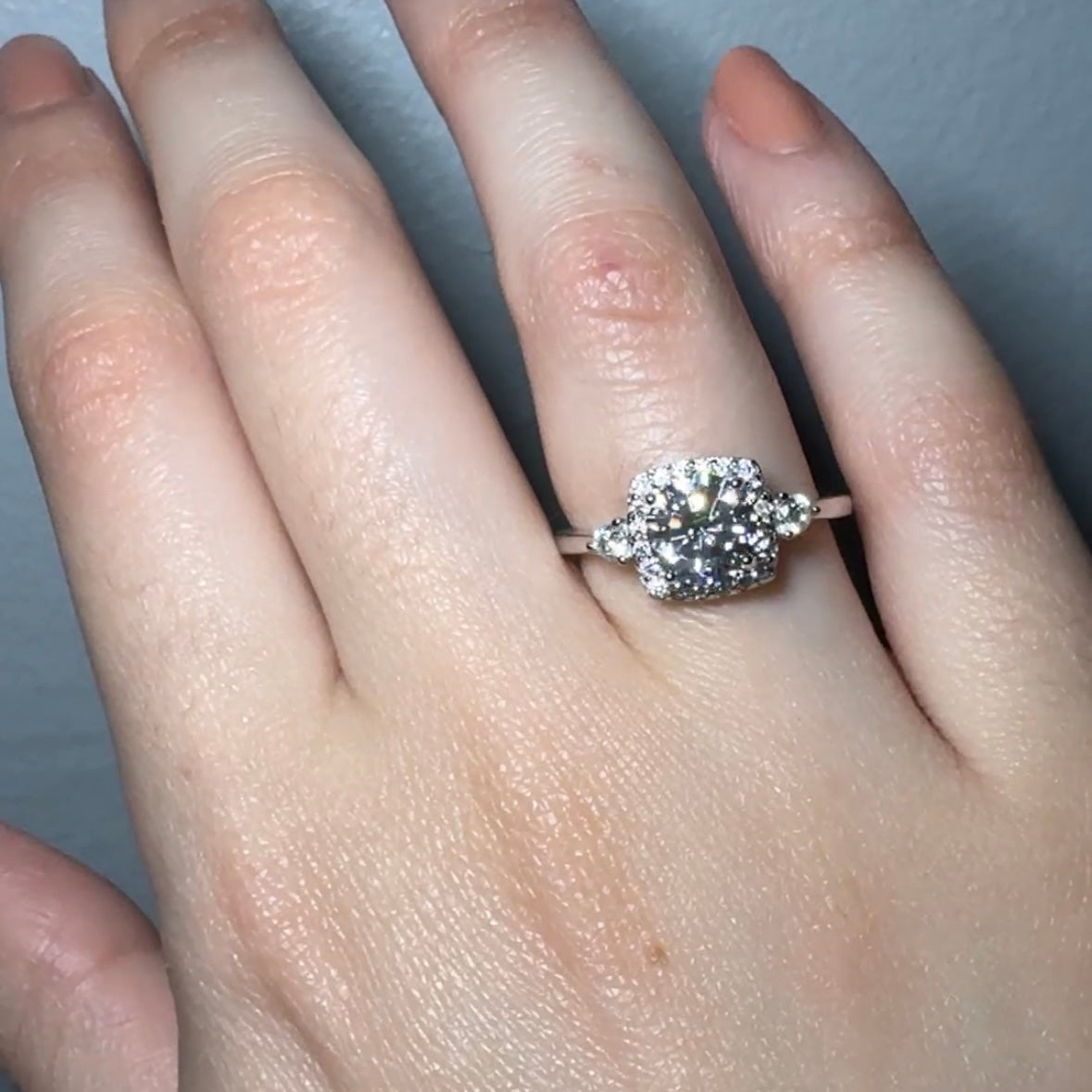 Model wearing Sterling silver ring with round white zirconia and a rectangular halo with round white zirconia around it. There is a round white zirconia on each side of the band.