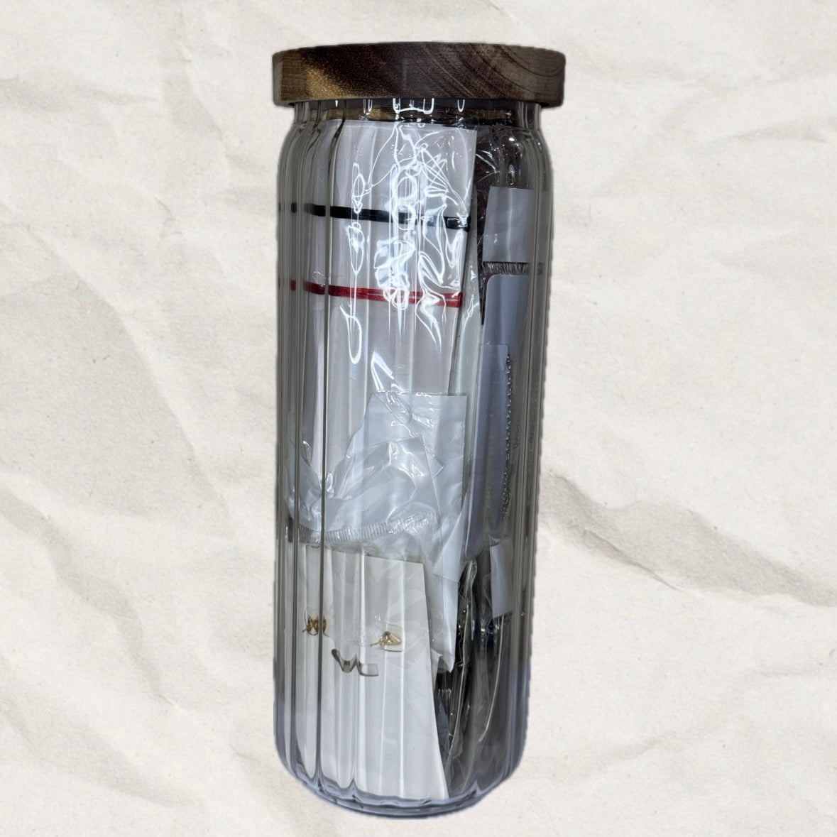 Large, clear tumbler with wooden lid on a white background. The tumbler is filled with jewelry.