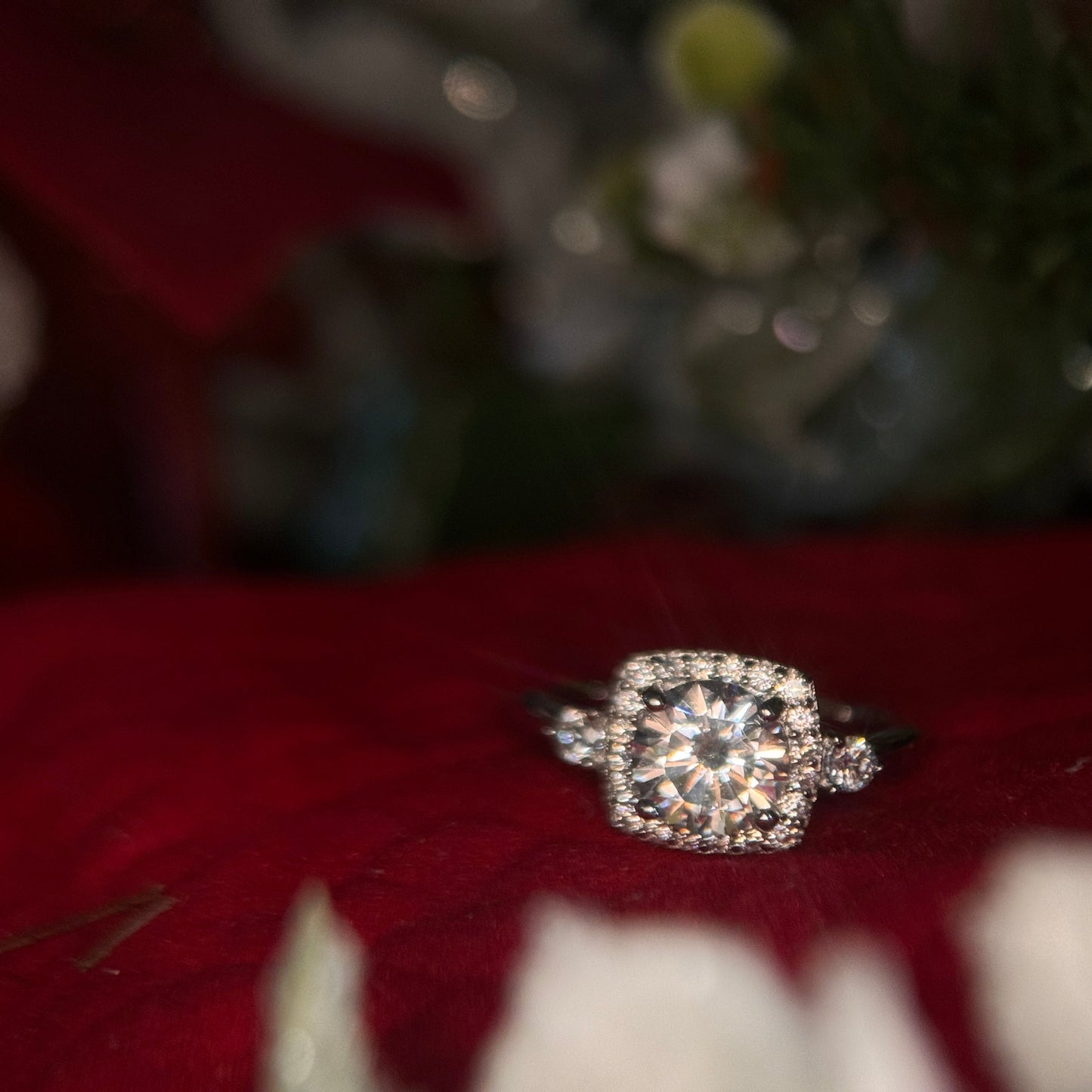 Sterling silver ring with round white zirconia and a rectangular halo with round white zirconia around it. There is a round white zirconia on each side of the band. The ring is on a red background.