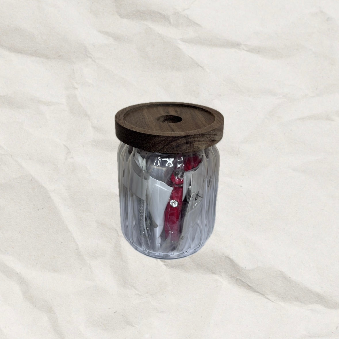Small, clear tumbler with wooden lid on a white background. The tumbler is filled with jewelry.