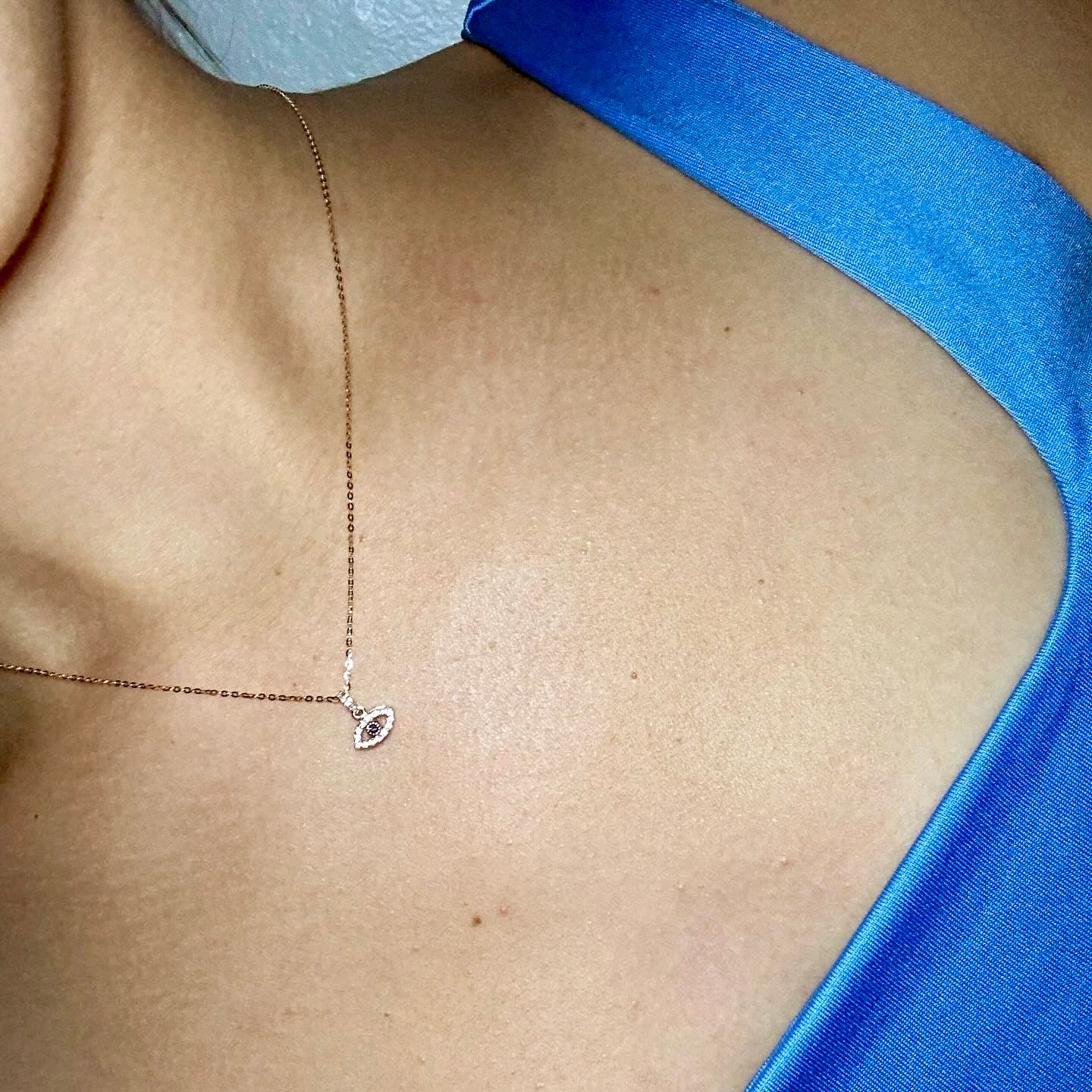 Model close up of chest wearing a yellow gold necklace with a yellow gold eye pendant that is outlined with white diamonds and has a blue sapphire in the center.