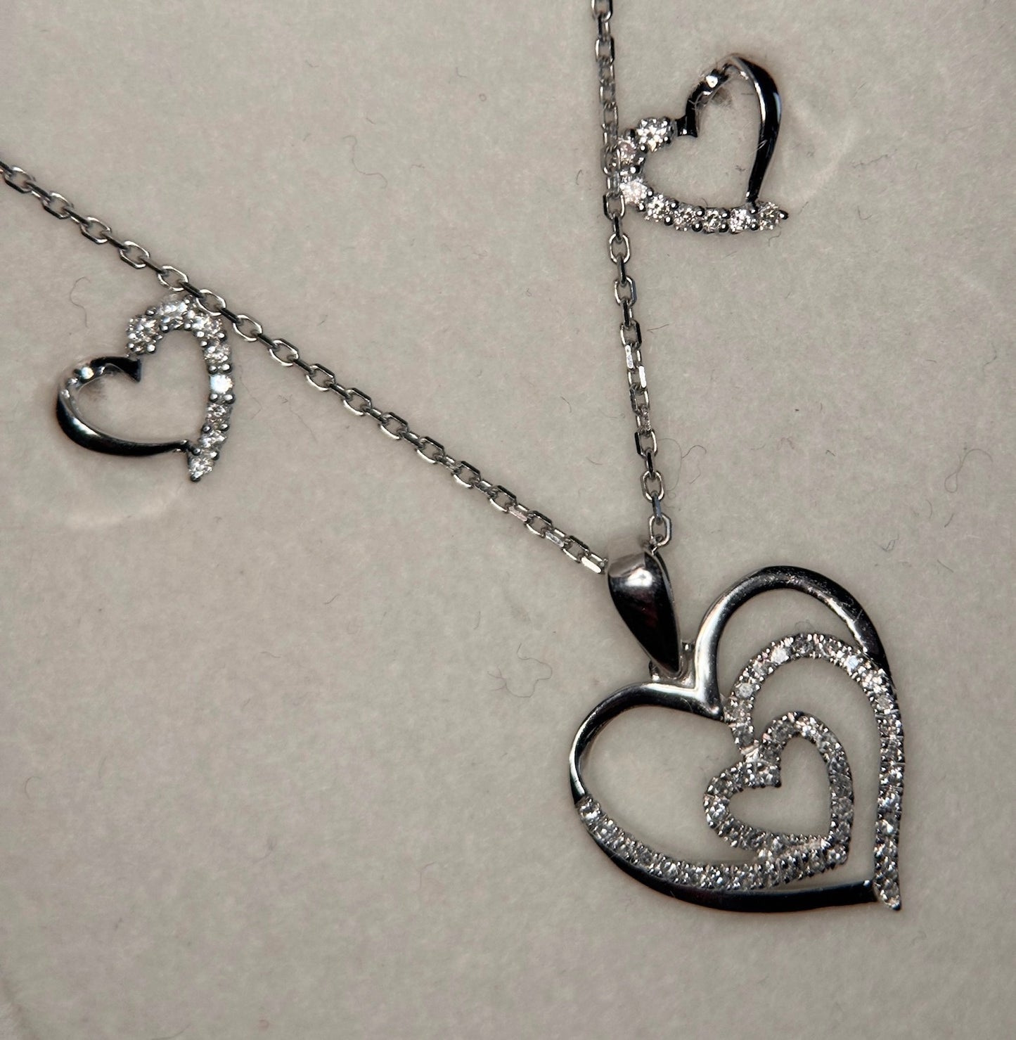 Zoomed in image of White gold heart set with white diamond. There are two heart studs with white accents on one side of the heart. And a heart pendant with a smaller diamond heart in the center.