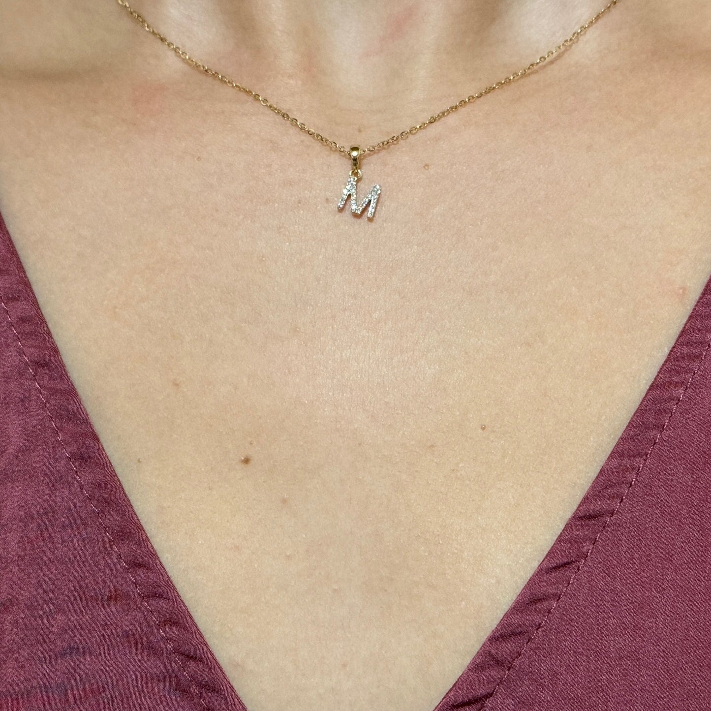 Close up of model wearing yellow gold M initial pendant outlined with white diamonds on a thin yellow gold chain.