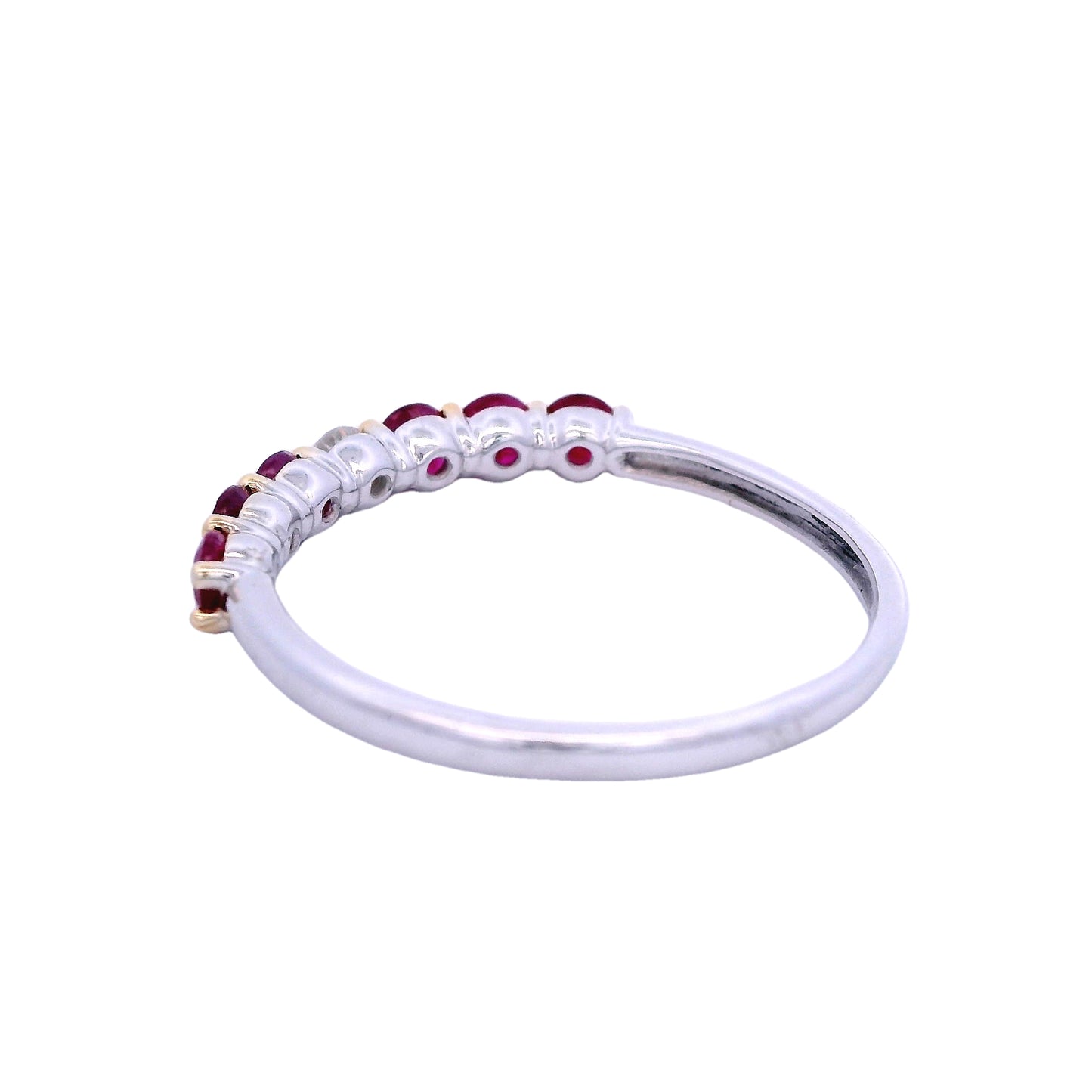 Angled back view of white gold ring. The band is smooth. In the center of the ring there is one round white diamond. On each side of the diamond there are 3 round dark pink rubies. The rubies and the diamonds are held together by yellow gold prongs.