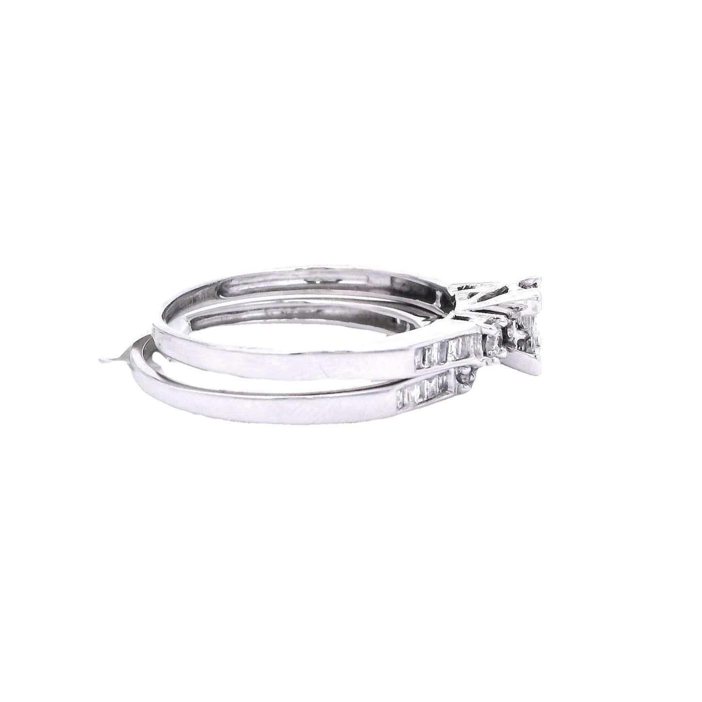 Side view of White gold bridal set. The center of the engagement ring is a princess cut made up of 4 square diamonds. On each side of the center of the ring, there is a single round diamond. The band has baguette diamonds towards the center. The wedding band has round diamonds in the center, and baguette diamonds on either side. It is laying under the engagement ring and fits perfectly.