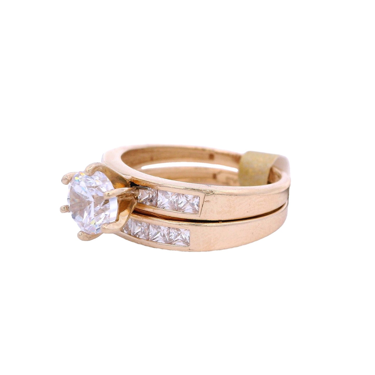Angled side view of yellow gold engagement ring and wedding band. The engagement ring has a round white zirconia in the center and white princess-cut zirconia on each side. The wedding band has white princess-cut zirconia in the center.