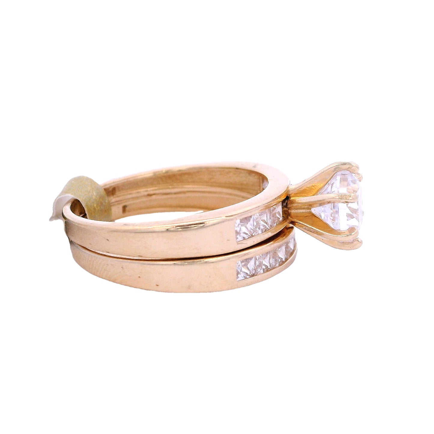 Side view of yellow gold engagement ring and wedding band. The engagement ring has a round white zirconia in the center and white princess-cut zirconia on each side. The wedding band has white princess-cut zirconia in the center.