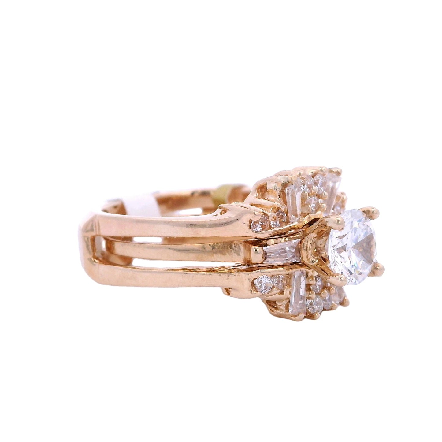 Angled view of gold bridal ring. The engagement band has a single white zirconia with a baguette zirconia on each side. The ring is inside a ring enhancer that has round and baguette white zirconia.