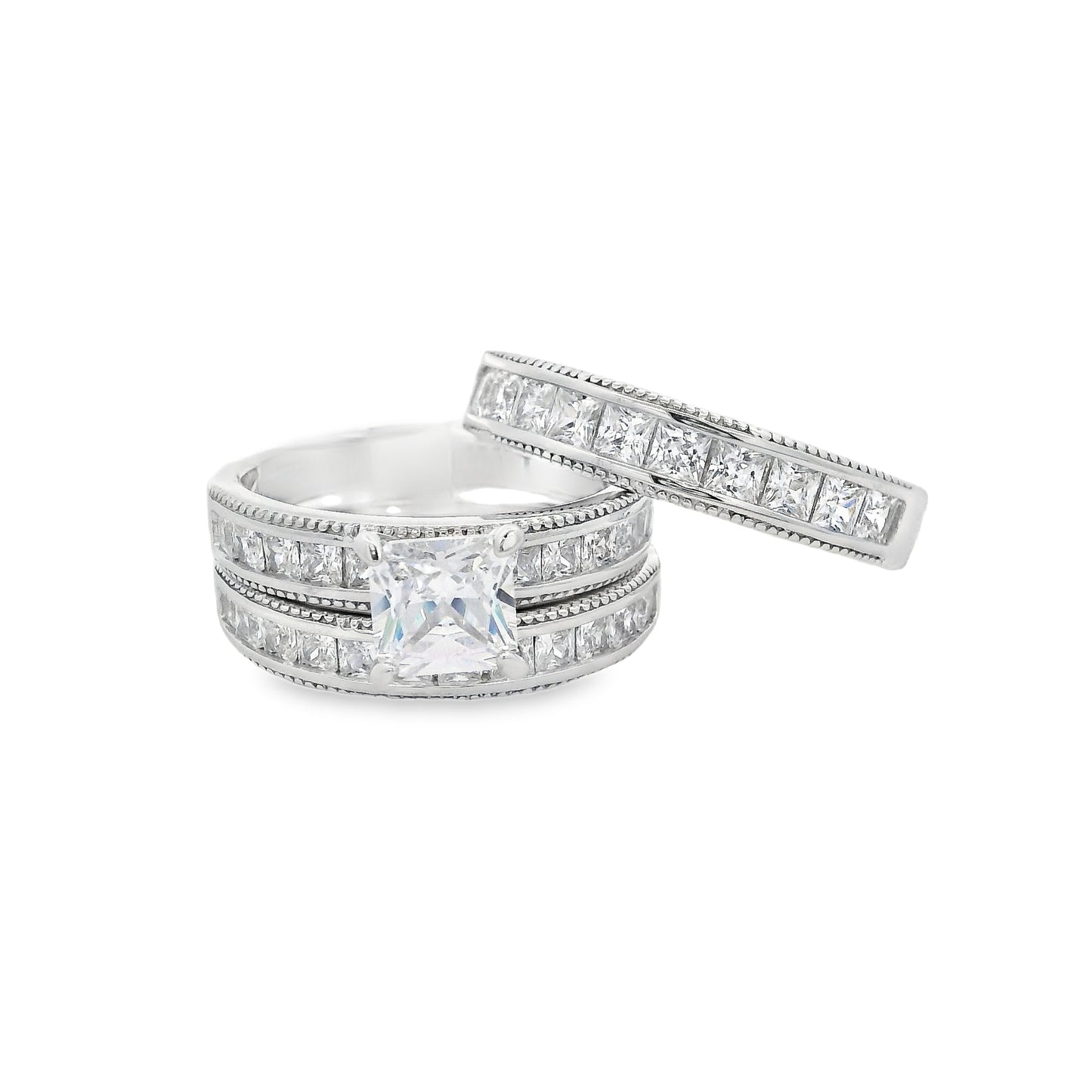 Front view of Silver bridal trio set. On the bottom there is a wedding band with square zirconia. On top is an engagement ring with a square zirconia in the center and smaller square zirconia on the sides. Laying on top at an angle is another wedding band that is thicker and with square zirconia.