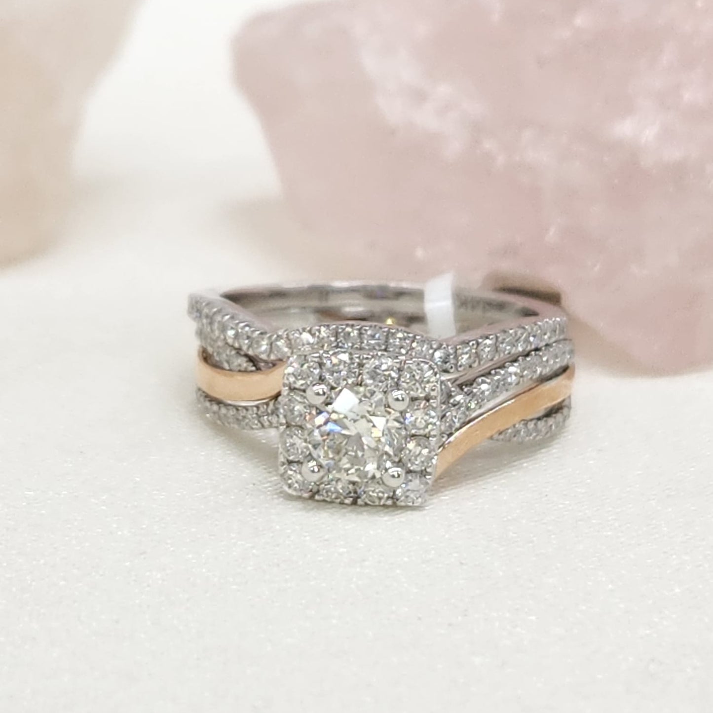 Front view of white and rose gold bridal set. The engagement ring is on the bottom. In the center of the ring there is a round diamond with a rectangular halo around it that has round white diamonds. The bands consist of 3 small bands: 2 of them are diamonds and 1 of them is rose gold. The wedding band traces the ring perfectly. It is laying above.