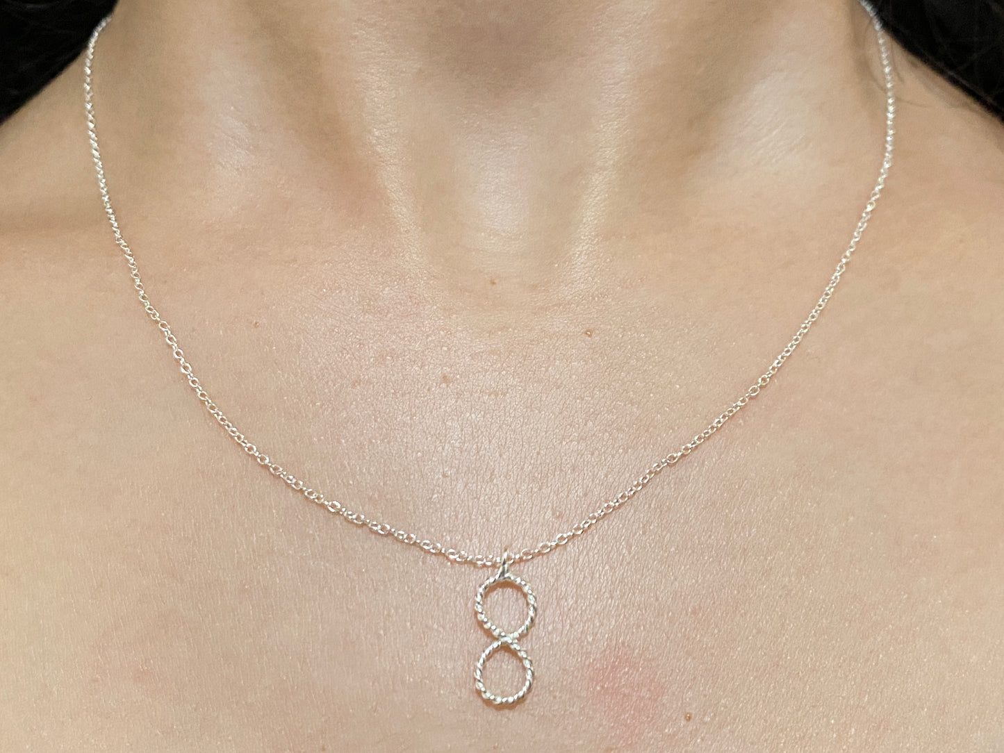 Silver vertical Infinity Pendant with rope texture and accompanying necklace. On model.