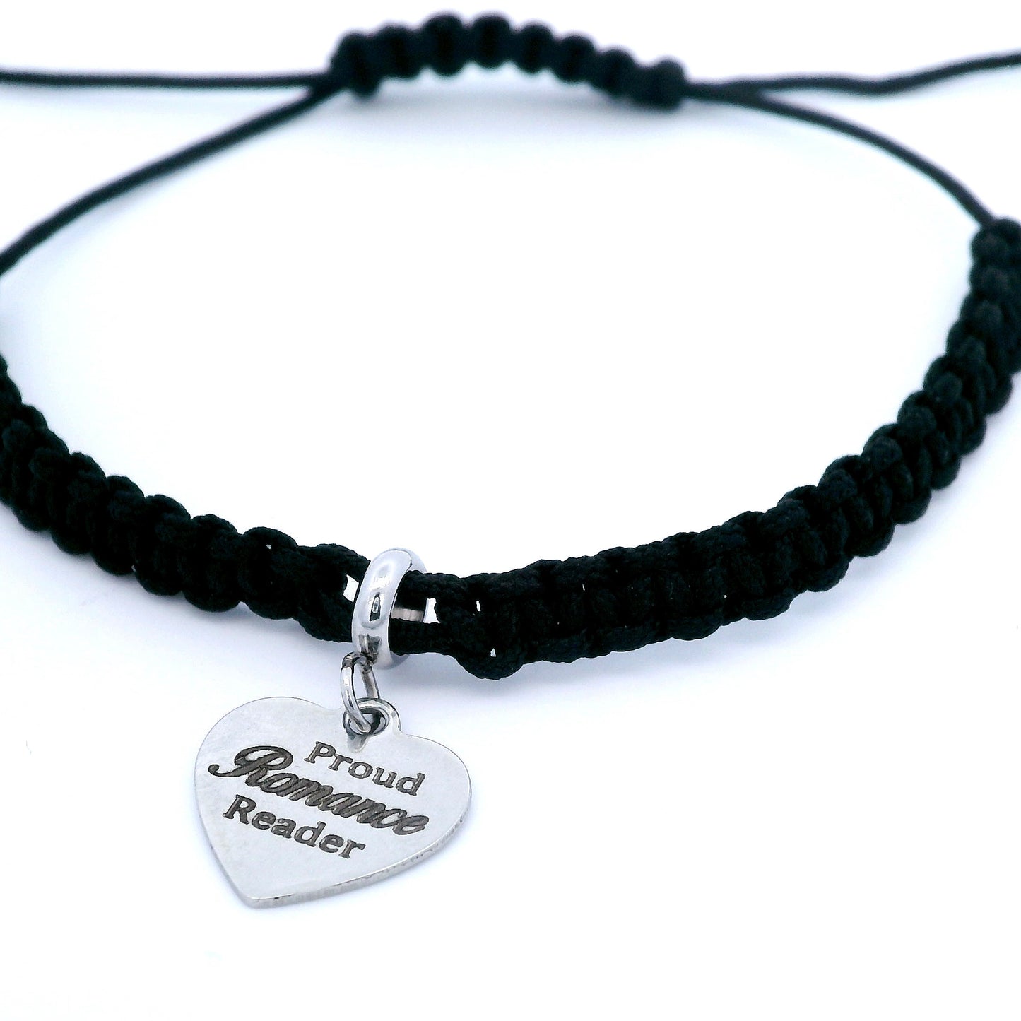 A black macrame bracelet bracelet with a silver heart-shaped charm engraved with 'Proud Romance Reader', shown on a clean white background.