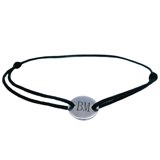 Black string bracelet with a round  stainless steel featuring the initials "B" and "M" in the middle on a white background