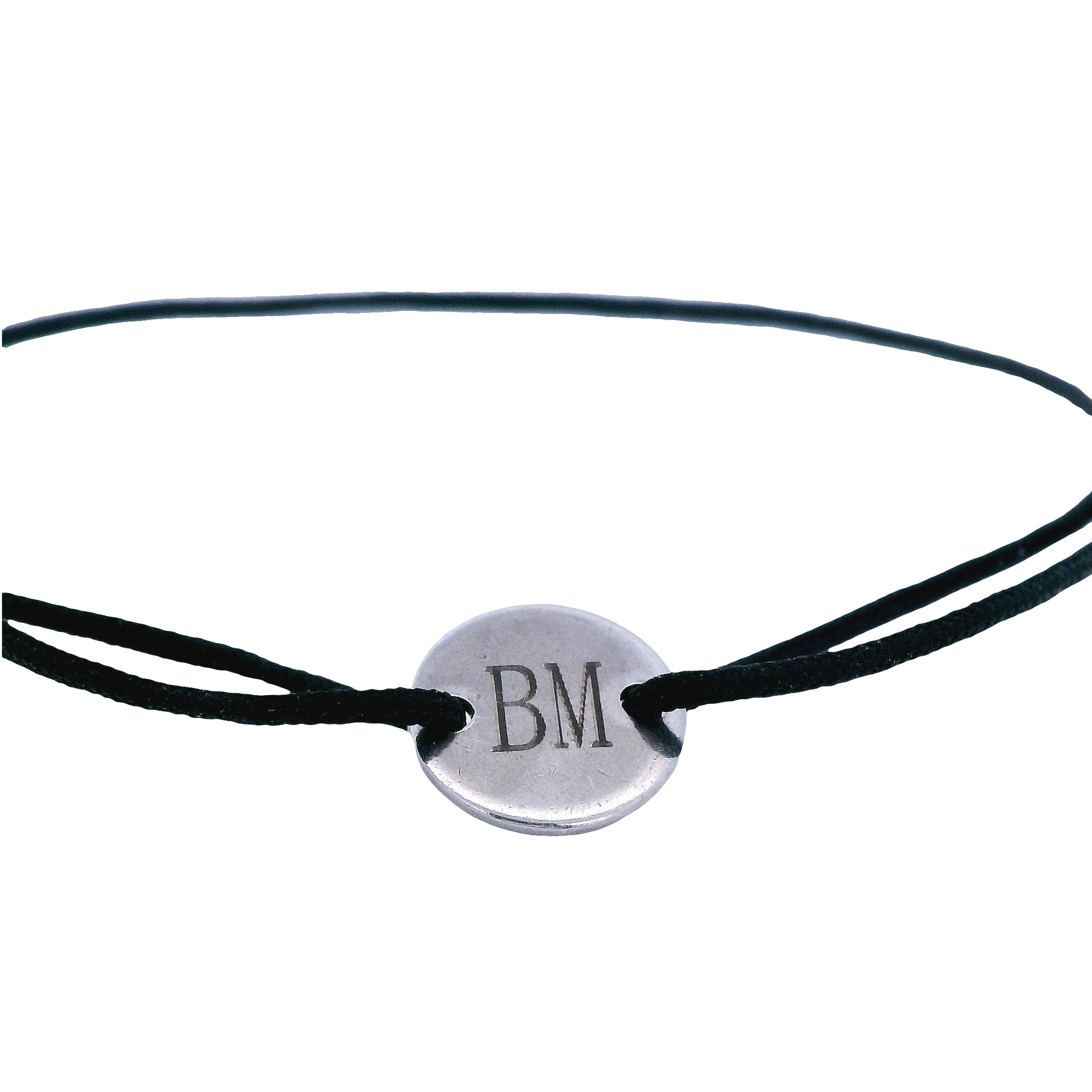 Close up of black string bracelet with a round  stainless steel featuring the initials "B" and "M" in the middle on a white background