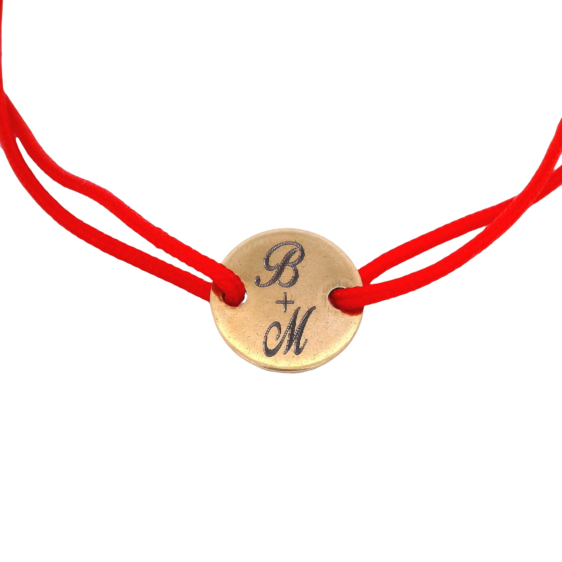 Close up of Red string bracelet with a round yellow stainless steel featuring the initials "B" and "M" with a plus sign in the middle on a white background