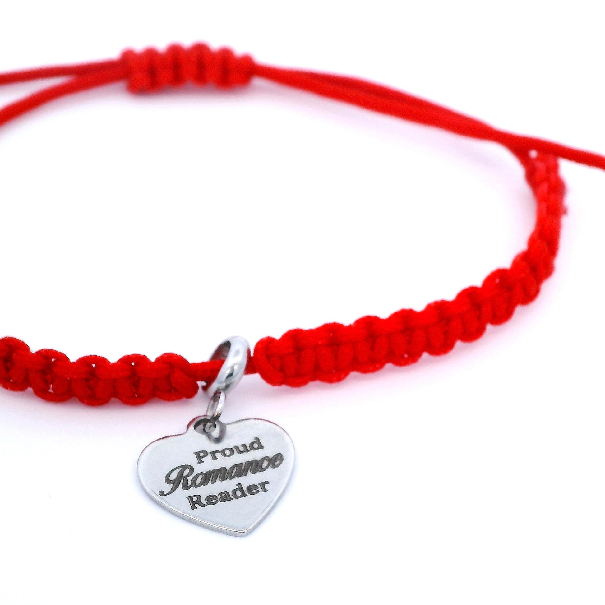 A red macrame bracelet with a silver heart-shaped charm engraved with 'Proud Romance Reader', shown on a clean white background.