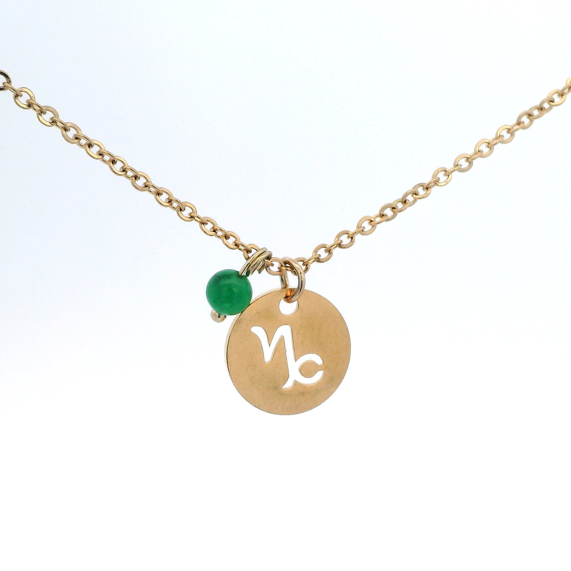 A gold-plated stainless steel chain necklace with a round gold disc pendant featuring a cutout symbol of the Capricorn zodiac sign, adorned with a small bead, on a white background.