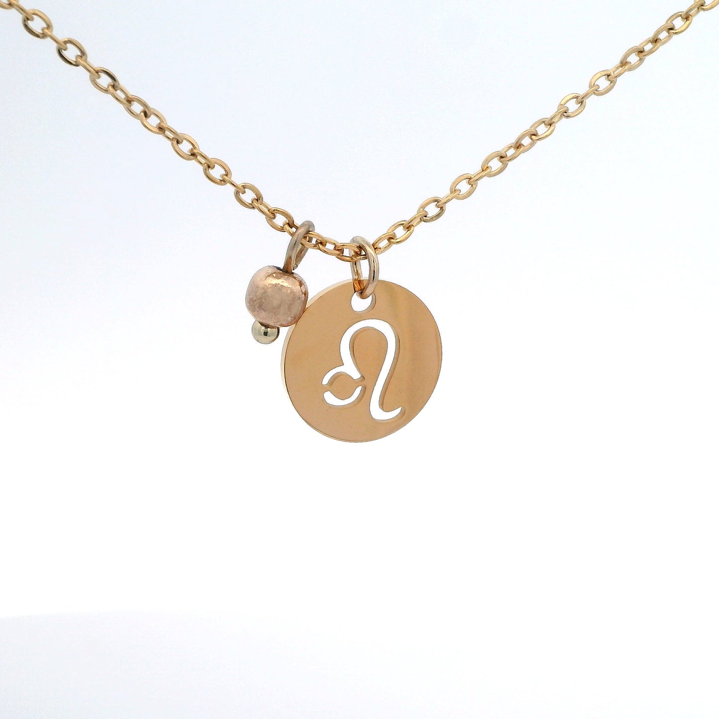 A gold-plated stainless steel chain necklace with a round gold disc pendant featuring a cutout symbol of the Leo zodiac sign, adorned with a small bead, on a white background.