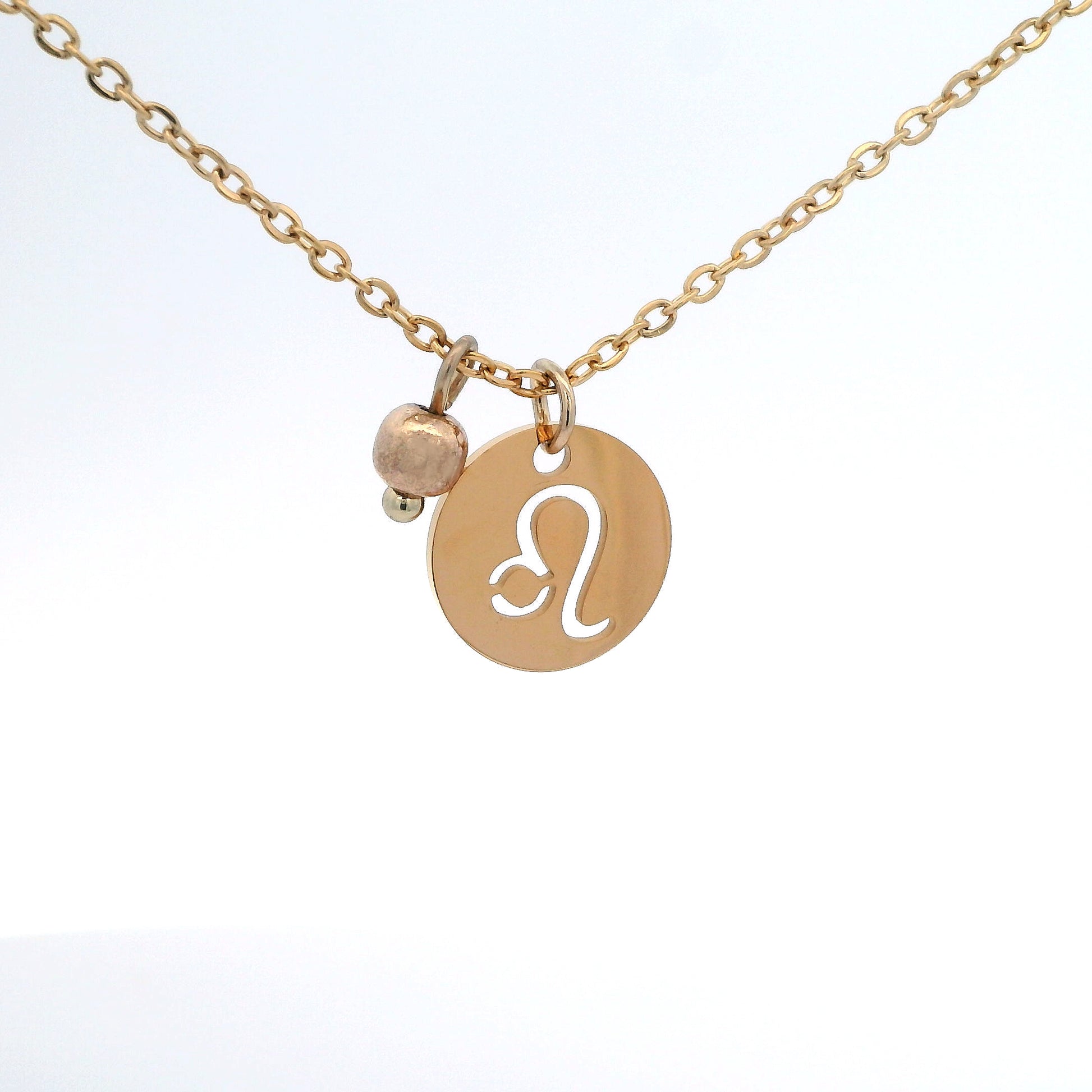 A gold-plated stainless steel chain necklace with a round gold disc pendant featuring a cutout symbol of the Leo zodiac sign, adorned with a small bead, on a white background.