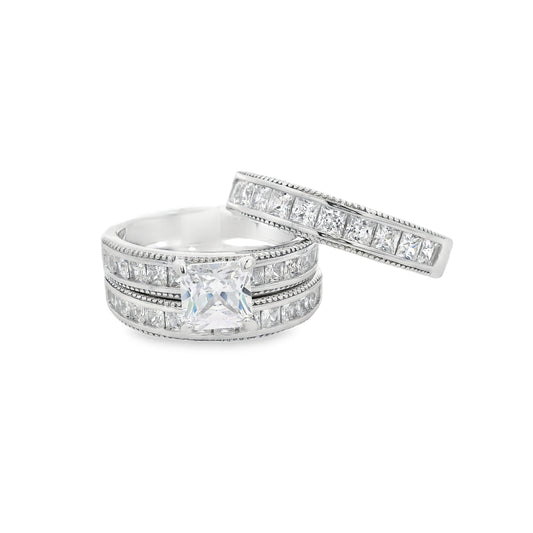 Front view of Silver bridal trio set. On the bottom there is a wedding band with square zirconia. On top is an engagement ring with a square zirconia in the center and smaller square zirconia on the sides. Laying on top at an angle is another wedding band that is thicker and with square zirconia.