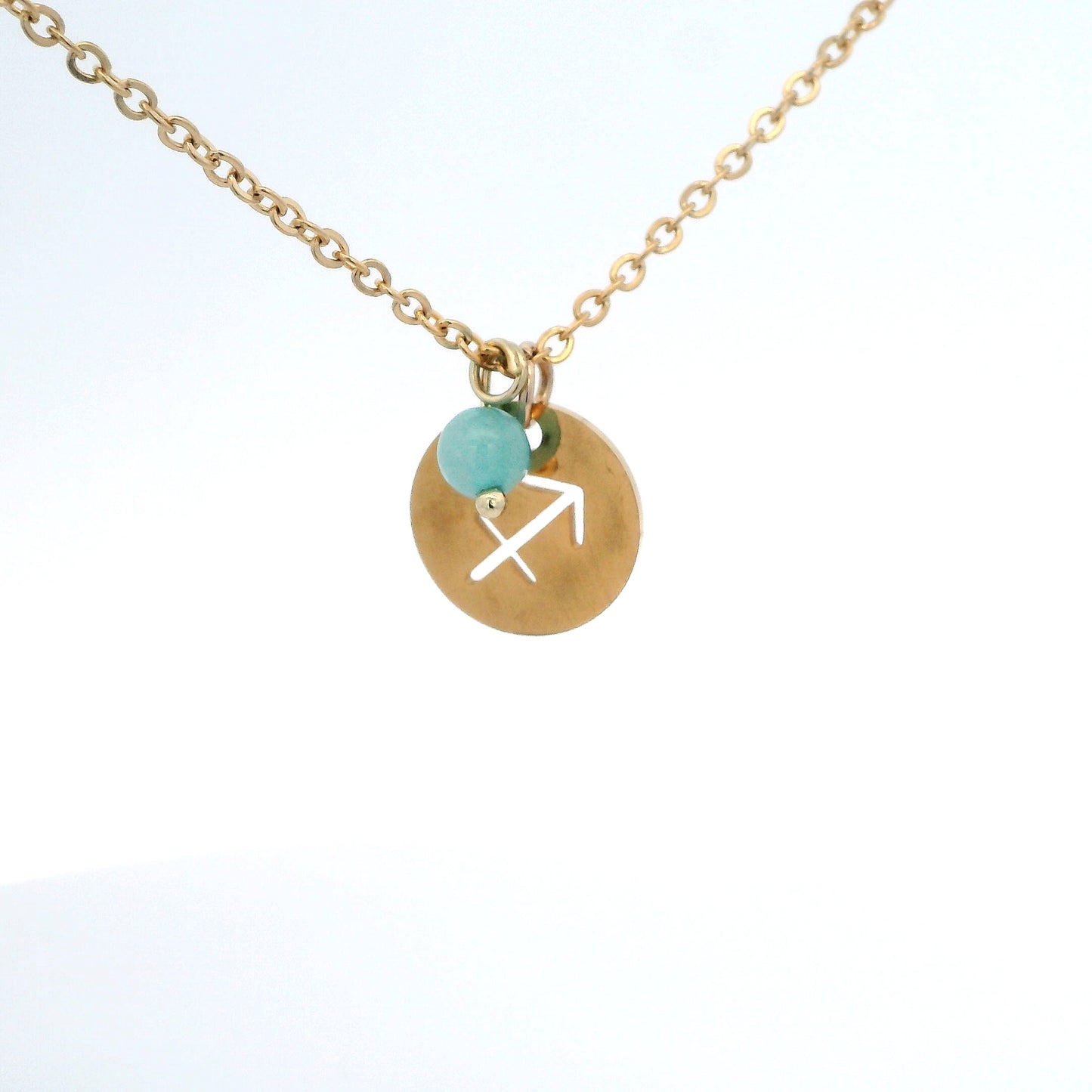 A gold-plated stainless steel chain necklace with a round gold disc pendant featuring a cutout symbol of the Sagittarius zodiac sign, adorned with a small bead, on a white background.