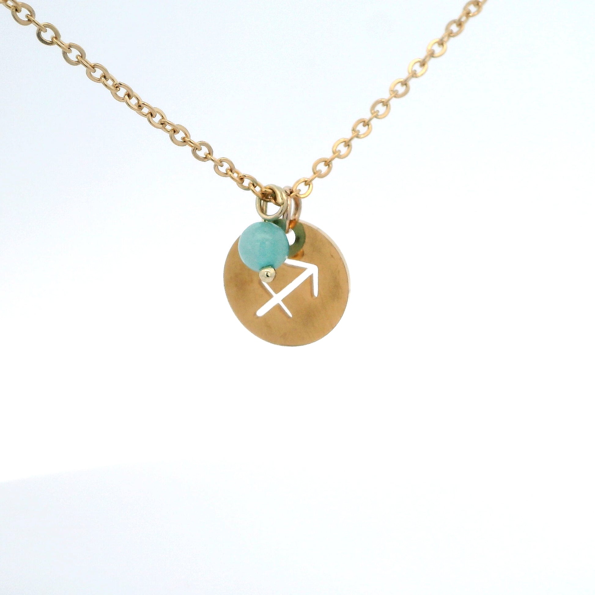 A gold-plated stainless steel chain necklace with a round gold disc pendant featuring a cutout symbol of the Sagittarius zodiac sign, adorned with a small bead, on a white background.